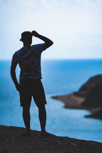 Rear view of man standing on rock by sea against sky