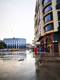 Wet street by buildings against sky in city