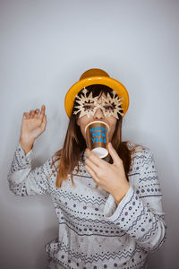 Portrait of woman holding cup against gray background