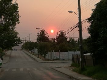 Road by trees against sky during sunset