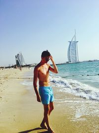 Full length of shirtless man standing on beach against clear sky