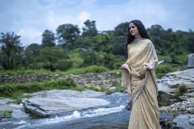 Woman standing by river against trees