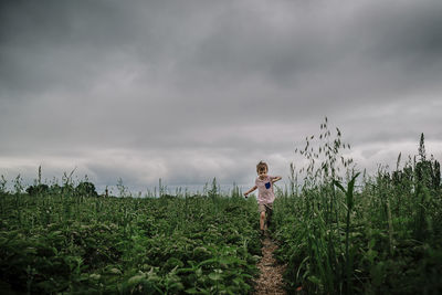 Boy running on field at farm against cloudy sky