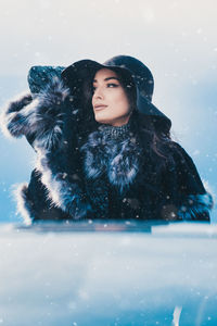Young woman wearing warm clothing looking away during snowfall