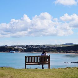 Rear view of woman sitting on bench looking at sea against sky