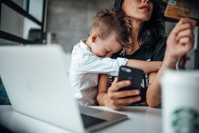 Son embracing mother shopping online through mobile phone at home