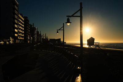 Silhouette city by sea against sky during sunset