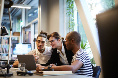 Male entrepreneurs explaining female bank manager over laptop at desk in creative office