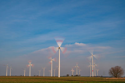 Low angle view of wind turbines on field against sky