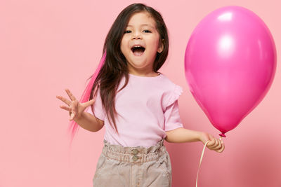 Portrait of young woman holding heart shape balloons against yellow background