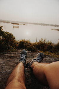 Low section of man relaxing on land against sky during sunset