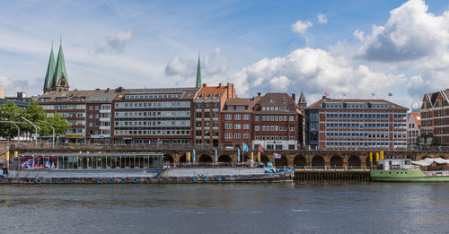 View of buildings by river against cloudy sky