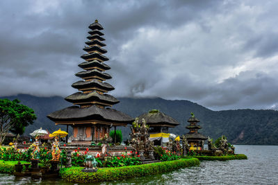 Temple by building against cloudy sky