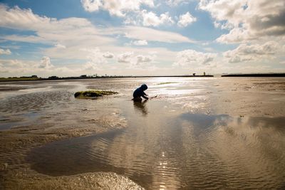 Side view of boy playing on shore at beach against sky