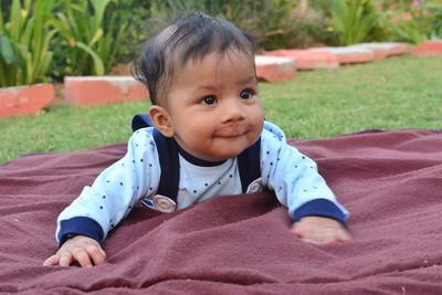 Cute baby boy looking away while lying on blanket in lawn