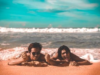 Portrait of man and woman lying on sand at beach against sky