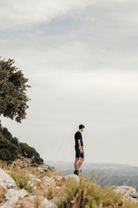 Full body side view of unrecognizable male hiker standing on rocky slope of mountain and observing landscape while travelling through highlands