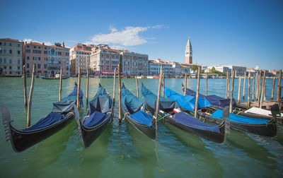 Gondolas moored in canal by buildings against sky