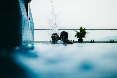 Couple kissing while swimming in pool against sky