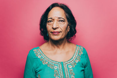 Portrait of confident senior woman with black short hair over pink background