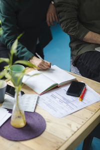 Midsection of man writing in book at desk