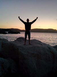 Full length of man standing on rock at sea shore against sky