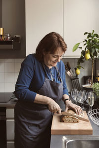 Smiling woman cutting bread in kitchen