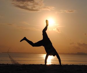 Silhouette man doing handstand on beach against sky during sunset
