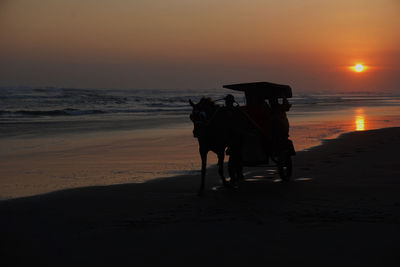 People riding horse at beach during sunset