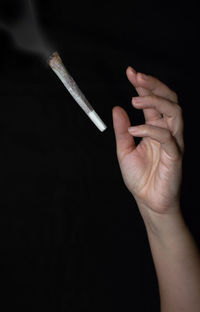 Close-up of hand throwing cigarette against black background