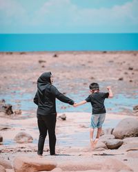 Rear view of woman holding hands with son at beach