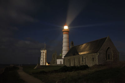 Illuminated lighthouse on field against sky at night