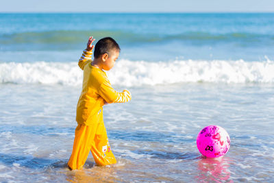 Side view of boy playing with ball at beach
