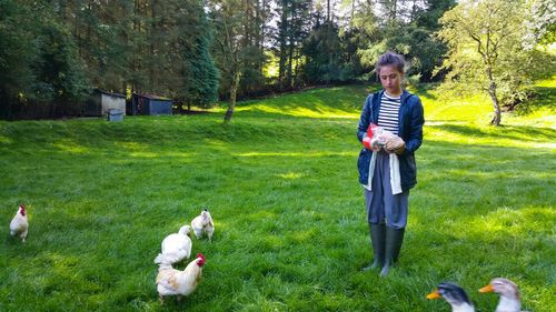 Young woman feeding chickens on grassy field at farm