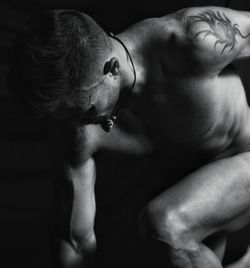 Naked muscular man posing against black background