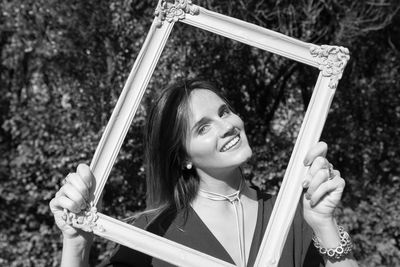 Portrait of smiling young woman holding frame in forest