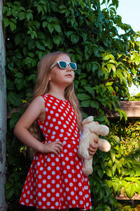 Beautiful happy girl in red polka dot dress soft toy on wooden balcony. cute joyful child long hair.