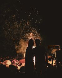 Silhouette man and woman standing by bonfire at night