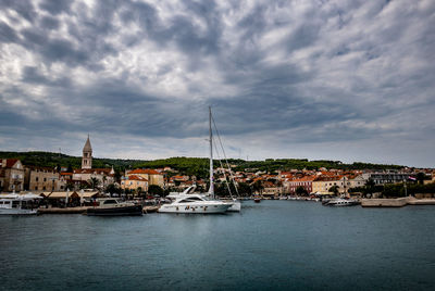 Sailboats moored in harbor by city against sky