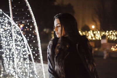 Woman with eyes closed standing by fountain at night