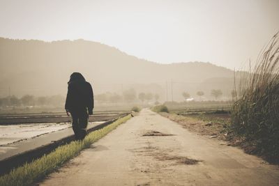 Rear view of man walking on road against sky