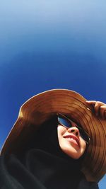 Close-up of woman wearing sunglasses and hat against clear sky