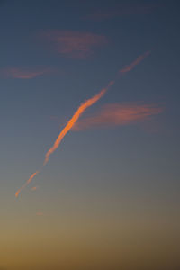 Low angle view of vapor trails in sky at sunset