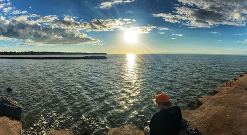 Rear view of man looking at sea against sky during sunset