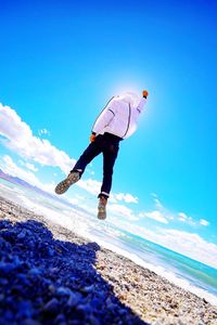 Full length rear view of man levitating at beach against blue sky