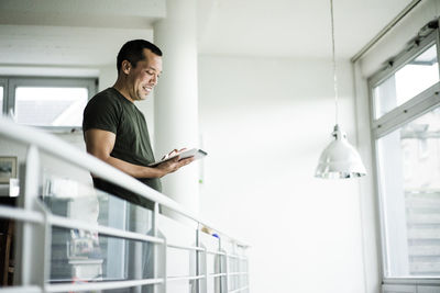 Smiling man at home using tablet on upper floor