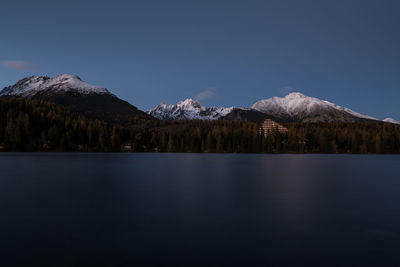 Scenic view of frozen lake in front of snowcapped mountains against clear blue sky