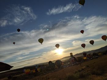 Hot air balloons flying over field against sky during sunset
