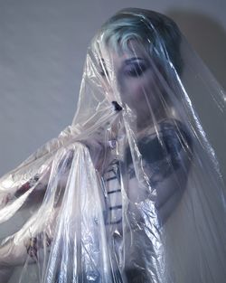 Young woman covered with plastic bag while standing against wall