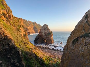 Scenic view of cliff by sea against clear sky